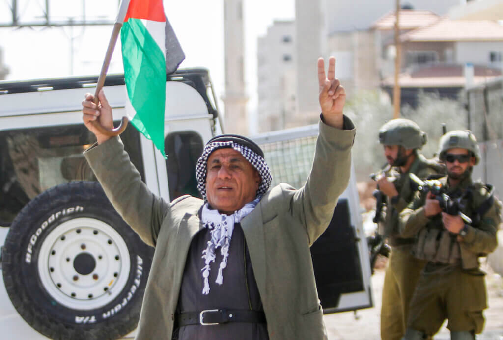 A man waves a Palestinian flag in front of Israeli forces to protest the siege of the West Bank town of Huwwara on March 2, 2023. (Photo: Mohammed Nasser/ APA Images)