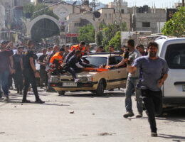 Crowds of Palestinians face off against invading Israeli forces at the entrance of Jenin refugee camp, while paramedics carry away injured youth on stretchers.
