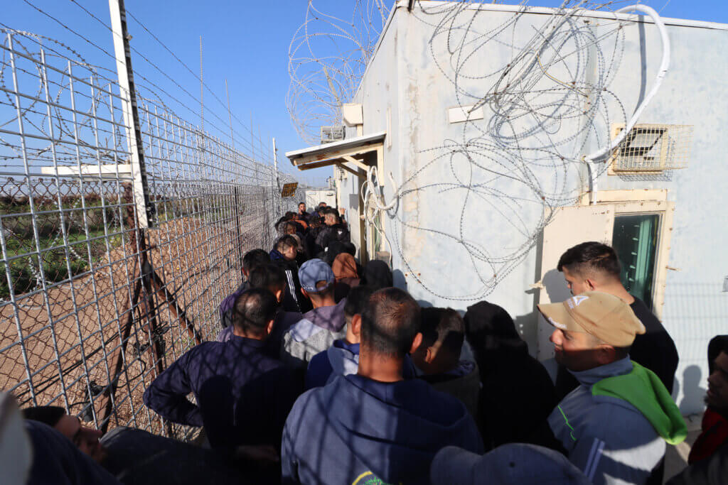 Palestinian farmers line up at an Israeli military gate in West Bank village of Hablah to reach their agricultural land located behind the Israeli colonial wall, in March 2023. (Photo: Ahmad Al-Bazz, Activestills)
