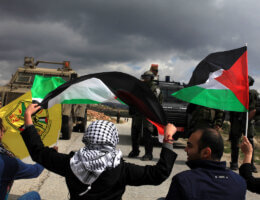 Palestinian protestors from the West Bank village of Nabi Saleh wave flags as they sit in the road in front of Israeli security forces during a demonstration against Jewish settlers near the Jewish settlement of Halamish on March 14, 2014. (Photo: Issam Rimawi/APA Images)