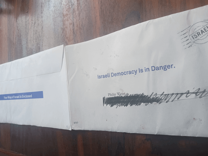 New Israel Fund fundraising envelope sitting on a table in April 2023. The envelope has Israel as its supposed postmark, and advertises Israel's "Democracy" and a free Israel map inside. 
