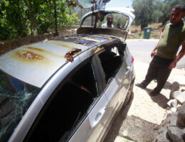 A damaged car with broken glass and a burnt roof is being inspected by Palestinians as it is parked in a driveway in the Palestinian village of Burqa, after a settler attack that burned several civilian vehicles in the village.