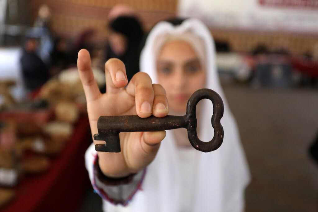 Photo showing a Palestinian girl holding up an old rusted key to a Palestinian home that was ethnically cleansed of its inhabitants in 1948.