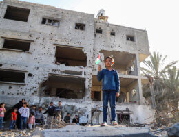 A Palestinian boy stands on the rubble of a building destroyed in an Israeli airstrike in Deir al-Balah, holding a Palestinian flag.