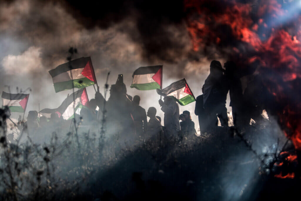 Silhouette of Palestnian protestors holding Palestinian flags with fire and smoke in the background, during a Palestinian "flag march" demonstration on the border with Israel, east of Gaza city, in response to the annual Israeli Flag March, May 18, 2023.