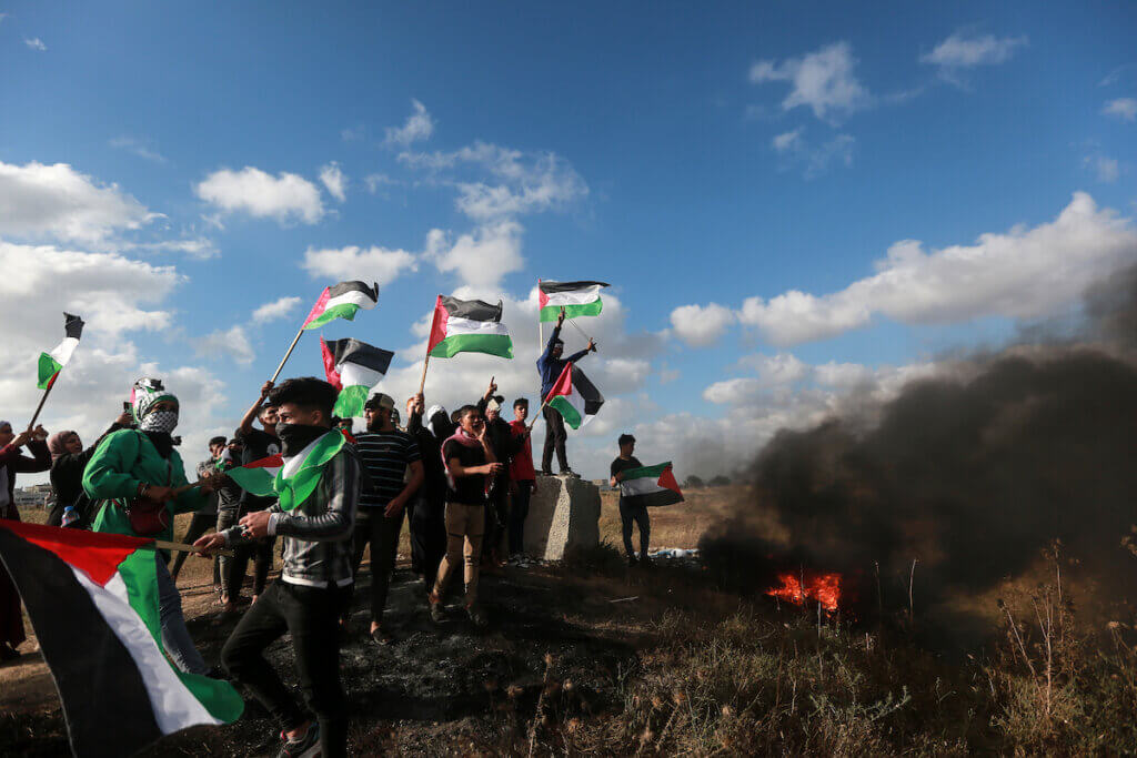 Palestinian protesters carry Palestinian flags, with burning tires and smoke to the side, during a Palestinian 