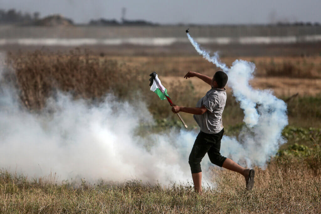 A Palestinian protester throws back a teargas canister in the direction of the Israeli army at the border between Gaza and Israel during a Palestinian 