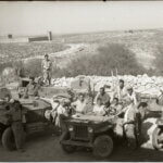 Historical photo from 1948 portraying the occupation of Iraq Suwaydan. Israeli soldiers are shown carrying rifles and riding their military jeeps as they pose for the camera, while in the background there is a stone fence and the plains of Iraq Suwaydan extending in the background, and the old British Police station can be seen in the distance.