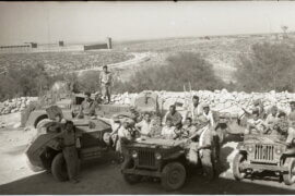 Historical photo from 1948 portraying the occupation of Iraq Suwaydan. Israeli soldiers are shown carrying rifles and riding their military jeeps as they pose for the camera, while in the background there is a stone fence and the plains of Iraq Suwaydan extending in the background, and the old British Police station can be seen in the distance.