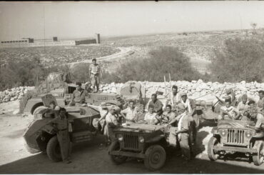 Historical photo from 1948 portraying the occupation of Iraq Suwaydan. Israeli soldiers are shown carrying rifles and riding their military jeeps as they pose for the camera, while in the background there is a stone fence and the plains of Iraq Suwaydan extending in the background, and the old British Police station can be seen in the distance.
