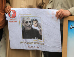 A close-up of a poster depicting Palestinian prisoner Walid Daqqah raising the victory sign during a court session, with the image of his daughter Milad superimposed in the background, and a line beneath the image that reads "Free the sick and imprisoned intellectual, Walid Daqqah."