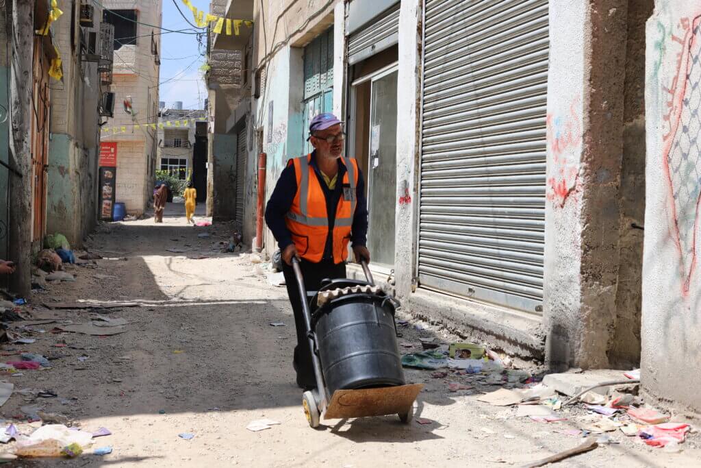 Mohammad Nimr, 49, is a local volunteer trying to keep the camp clean. He doesn’t work for UNRWA’s sanitation department, but most days you can find him with his broom, pale, and trash can, picking up trash from the street. (Malik Hamamra/Mondoweiss) Aida refugee camp, occupied West Bank, May 2023.