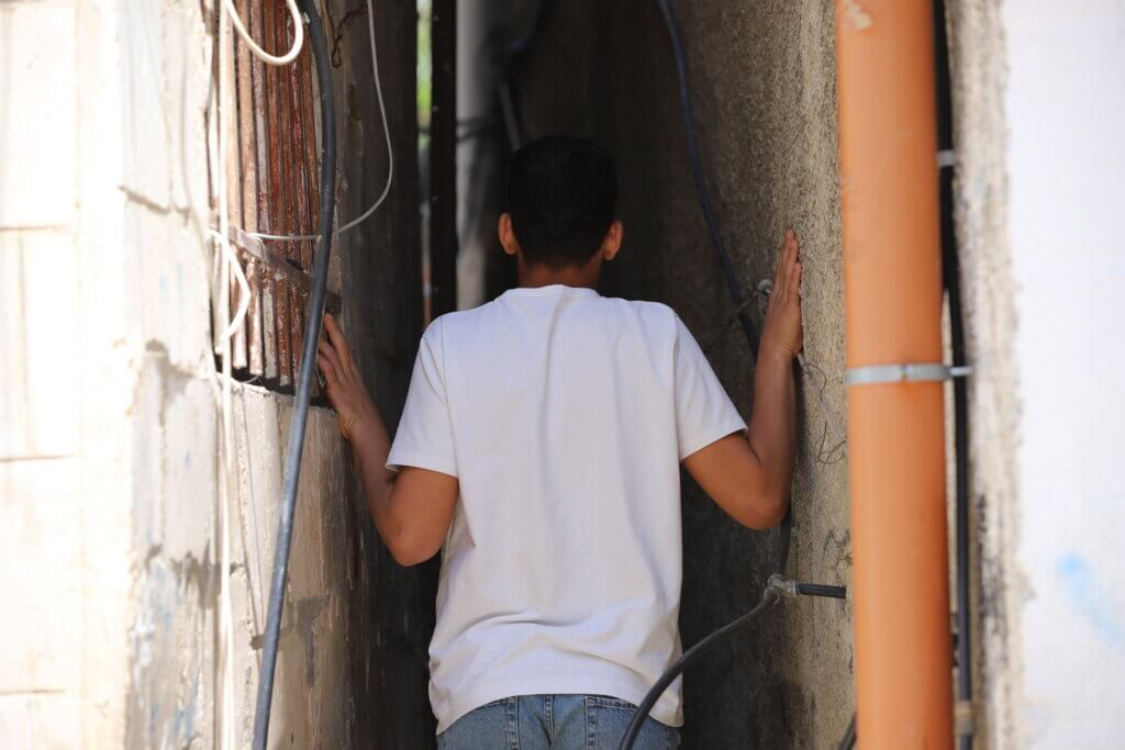 A Palestinian teenage boy walks fown a narrow alleyway in the Aida refugee camp. The camp is home to more than 6,000 people, living in an area of less than 0.01 square kilometers, making it a cramped and crowded place. Many of the homes in the camp are extremely close together, meaning that residents receive little privacy inside their own homes. (Malik Hamamra/Mondoweiss) Aida Refugee Camp, occupied West Bank, May 2023.