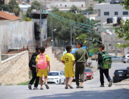 A group of boys walk home from school, next to the Israeli apartheid wall that runs along the Aida refugee camp. (Malik Hamamra/Mondoweiss) Aida Refugee Camp, occupied West Bank, May 2023.