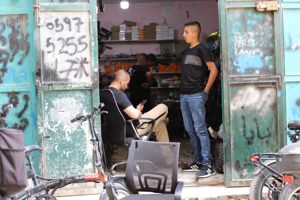 Two young men hang out in a local repair shop in the Aida refugee camp.  (Malik Hamamra/Mondoweiss) Aida Refugee Camp, occupied West Bank, May 2023.