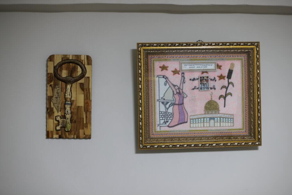 A wooden carving of a key, and a framed artwork depicting the Al-Aqsa mosque on the wall of Mazyouna Abu Srour's home. 