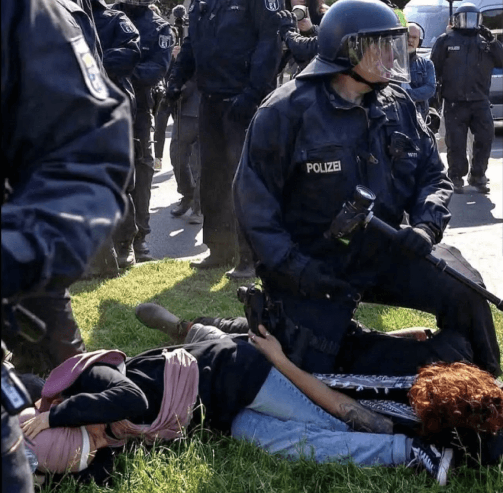 German policeman kneeling on the back of a protester at a Nakba rally in Berlin.