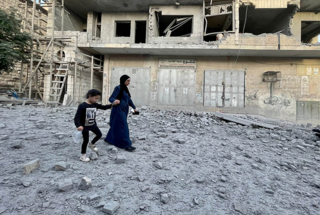 A woman holding hands with a little girl walks across the rubble-strewn street outside a bombed-out apartment detonated by the Israeli army in the Old City of Ramallah.