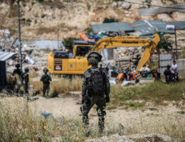 An Israeli soldier stands guard as bulldozers carry out a demolition operation in the background in the Jabal Mukaber neighborhood of East Jerusalem, May 10, 2023.