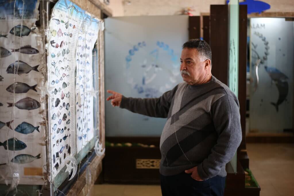 Asad Abu Hasirah, a seafood restaurant owner in Gaza, points to a large poster displaying different types of fish and their respective names.