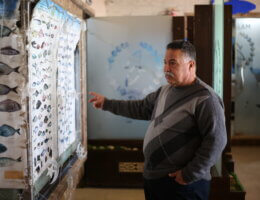 Asad Abu Hasirah, a seafood restaurant owner in Gaza, points to a large poster displaying different types of fish and their respective names.