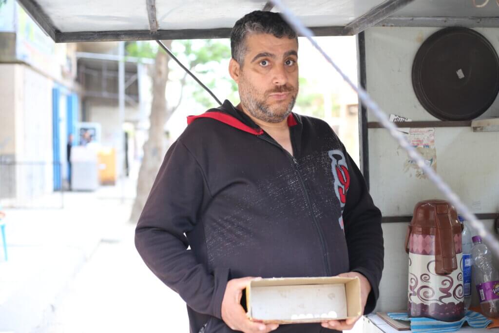 Ameen Qaddoum, 50, holds up a box containing all the money he made that today from his cart selling coffee and tea. There are only a meager 7 shekels in the box.