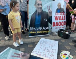 Milad Daqqa, left, standing next to a poster depicting her father, Walid Daqqa, holding up the victory sign with the sentence "Free Walid Daqqah" at the bottom, at a rally calling for his freedom.