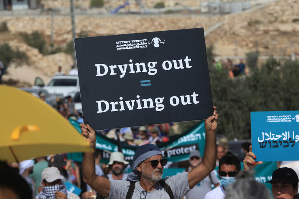 An Israeli activist carries a sign that reads "Drying out = Driving out" during a demonstration against Israeli land confiscation and the cutting of water supply for Palestinians villages in the southern area of the West bank town of Hebron, on October 2, 2021.