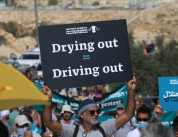 An Israeli activist carries a sign that reads "Drying out = Driving out" during a demonstration against Israeli land confiscation and the cutting of water supply for Palestinians villages in the southern area of the West bank town of Hebron, on October 2, 2021.