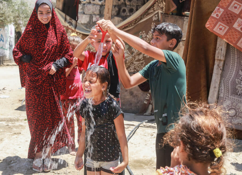 Palestinian children cool themselves off during a heat wave in Gaza, July 2023. The children are pouring water over each others' heads.