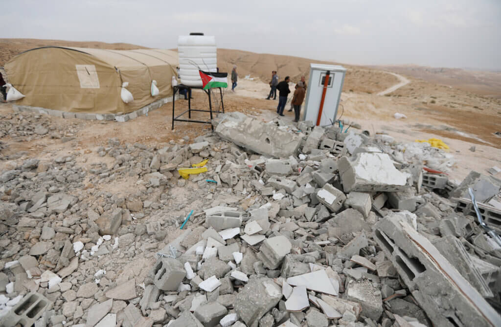 Palestinians inspect the ruins of a school in Isfey al-Fauqa in Masafer Yatta. A Palestinian flag is perched atop the rubble in the distance.