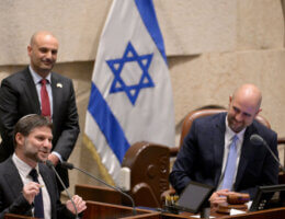 Finance Minister Bezalel Smotrich speaking at a podium in the Knesset, with the Israeli flag behind him.