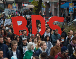 A group of solidarity protesters hold up a BDS sign at a rally in Berlin, alongside placards that read "Jewish Anti-Fascist Action" and "Jews for BDS."