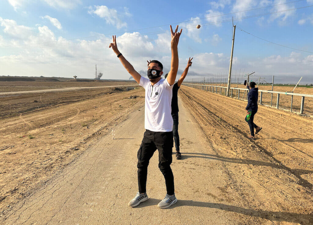Palestinians after crossing the border fence with Israel from Khan Yunis in the southern Gaza Strip on October 7, 2023. A Palestinian with a mask raises the "V" sign as he crosses the border fence.