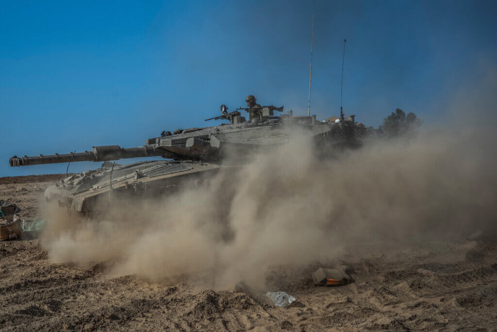 An Israeli tank moves through the desert and is shrouded by dust.