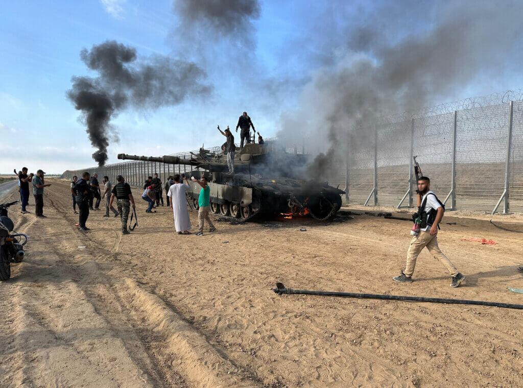 Members of the Ezz Al-Din Al Qassam Brigades, the military wing of Hamas, burn an Israeli military armored vehicle outside the Gaza Strip, October 7, 2023. (Photo: Stringer/APA Images)