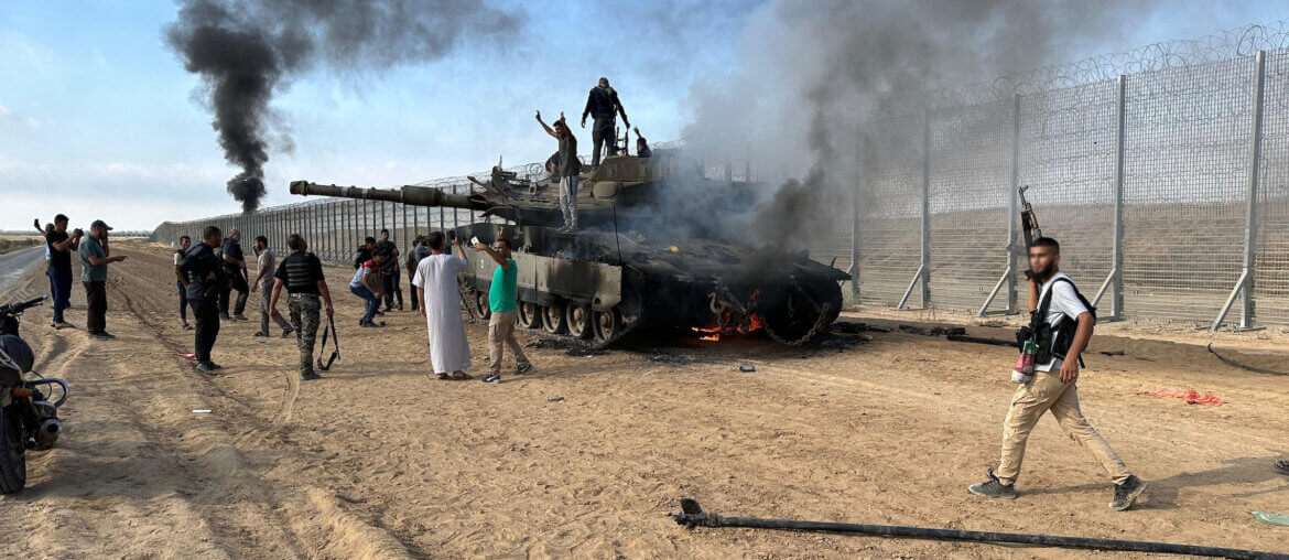 Members of the Ezz Al-Din Al Qassam Brigades, the military wing of Hamas, burn an Israeli military armored vehicle outside the Gaza Strip, October 7, 2023. (Photo: Stringer/APA Images)