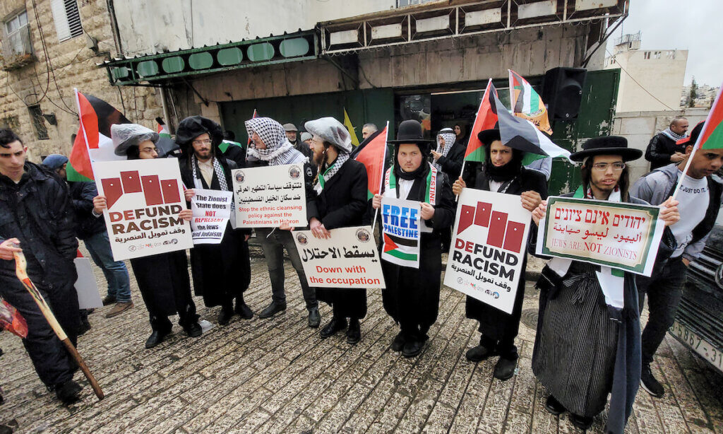Neturei Karta members hold placards during an annual demonstration in memory of the 1994 Ibrahimi Mosque massacre, near a gate leading to Hebron's main al-Shuhada street, Feb. 25, 2022. (Photo: Mamoun Wazwaz/APA Images)