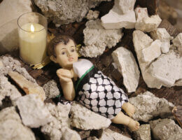 Palestinians light a candle near a statue showing a figure symbolizing the child Jesus lying amid the rubble in a cave, before Christmas at the Evangelical Lutheran Church, in Bethlehem, on December 08, 2023. (Photo: Mamoun Wazwaz/APA Images)
