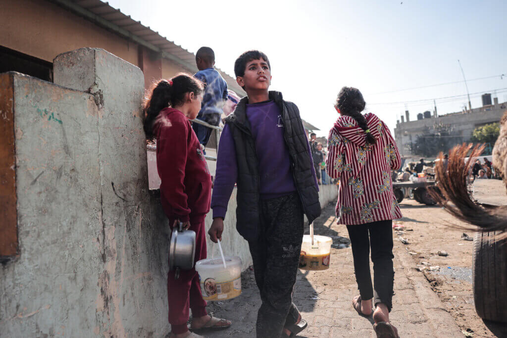 A Palestinian boy carries food in plastic buckets at a donation point in Rafah Gaza.