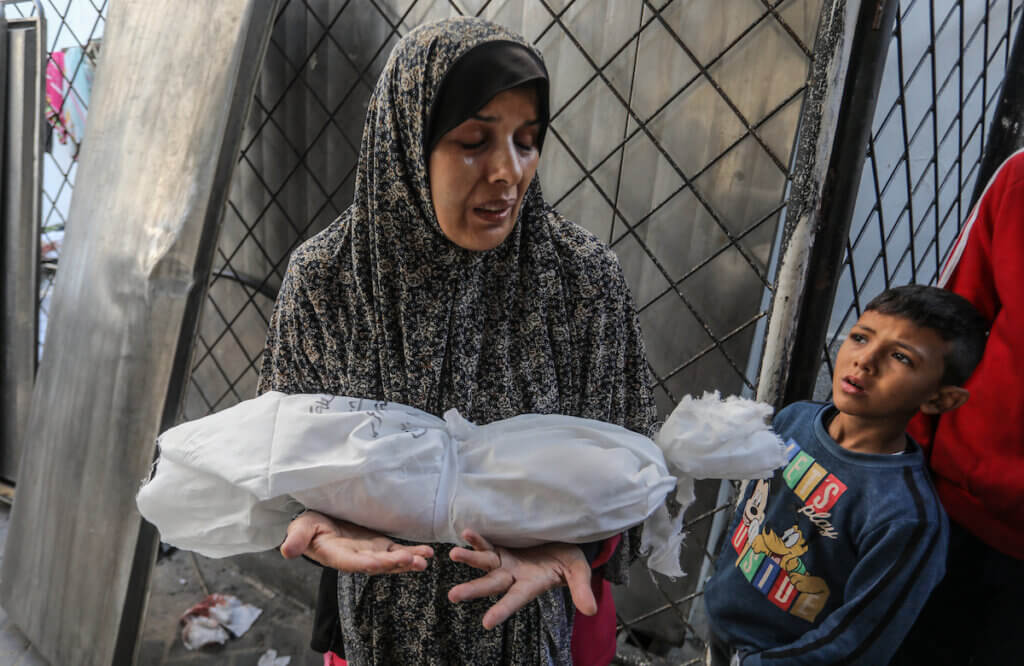 A Palestinian woman carries the shrouded body of her slain infant, who was killed by Israeli bombardment, December 19, 2023. (Photo: © Abed Rahim Khatib/dpa via ZUMA Press/APA Images)