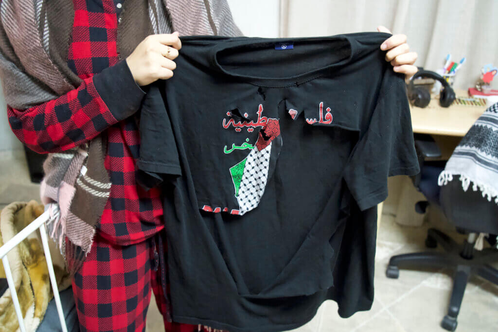 Yumna Amira holding her 13-year-old brother Mohammad's shirt that Israeli soldiers slashed while it was still on his body because it had a map of Palestine on it. (Photo: Leila Warah)