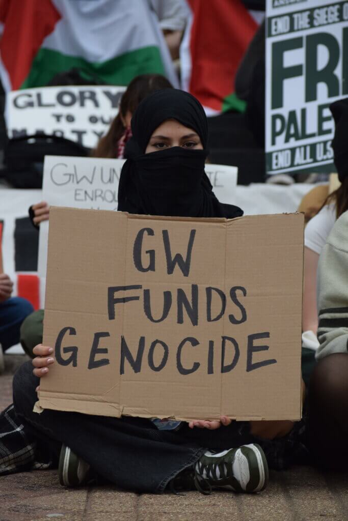 Student holds a sign reading "GW FUNDS GENOCIDE" at a Kogan Plaza Sit-In on Nov. 9. (Photo: Jelina Liu)