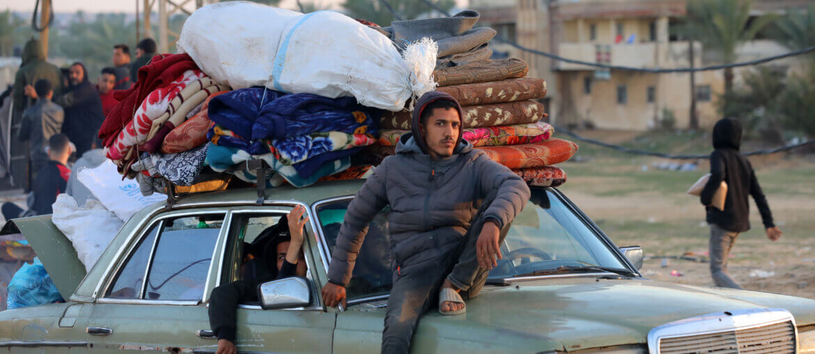 A Palestinian man sits on a car transporting blankets, mattresses, and other belongings of displaced Palestinians in the Gaza Strip.
