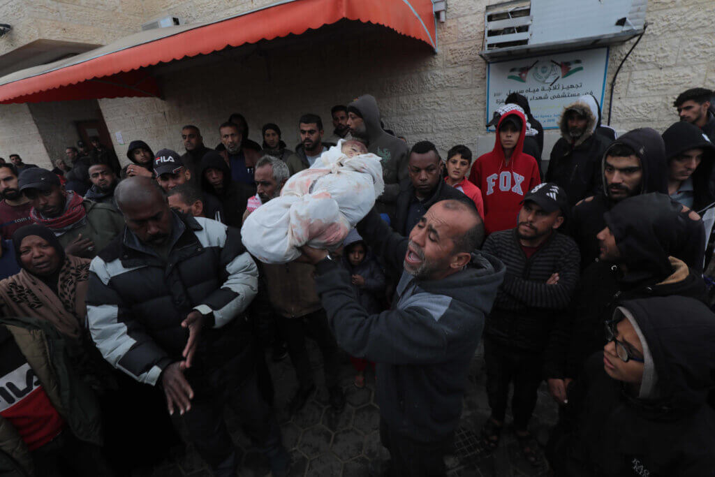 A grief-stricken Palestinian man holds up the shrouded body of a dead child in Gaza amidst a crowd outside the mortuary of the Al-Aqsa Hospital in central Gaza.