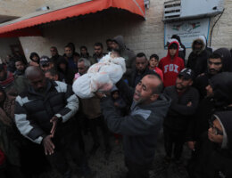 A grief-stricken Palestinian man holds up the shrouded body of a dead child in Gaza amidst a crowd outside the mortuary of the Al-Aqsa Hospital in central Gaza.