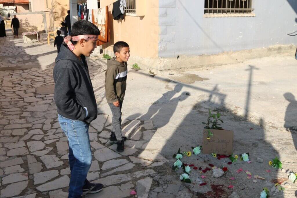 Young boys stand around the memorial for slain Palestinians in Tulkarem. Flowers are placed around the blood-soaked pavement where three young Palestinian men were assassinated by Israeli forces. 