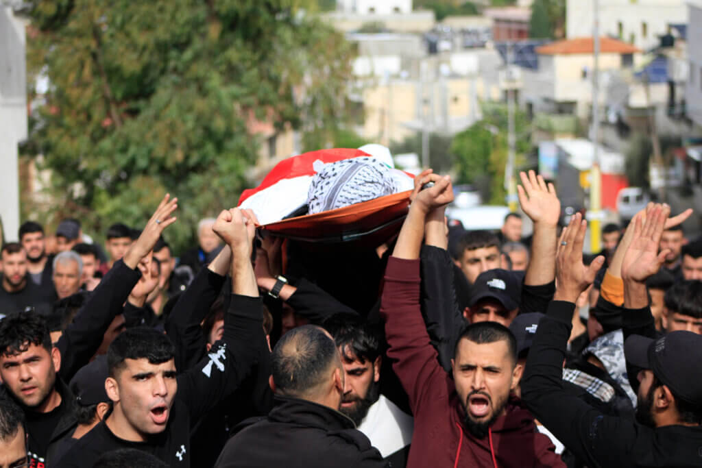 Mourners carry the flag-draped body of 17-year-old Mahmud Bassem Abu Haniyeh, killed in an Israeli raid on the occupied West Bank town of Azzun, during his funeral on December 10, 2023. (Photo: Mohammed Nasser / APA Images)