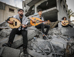 Palestinian youths play music on the rubble of destroyed houses in Deir al-Balah destroyed in an Israeli airstrike on May 13, 2023. (Photo: Abdelrahman Alkahlout/APA Images)