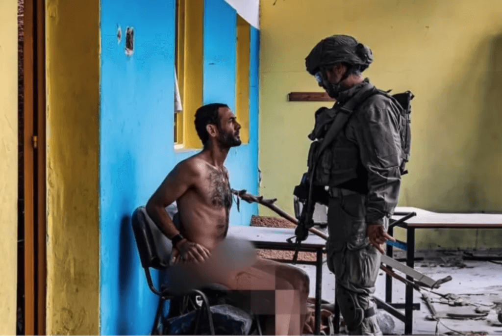 An already iconic image showing an Israeli soldier interrogating a Palestinian man in Gaza. There are signs the man had been tortured and he has a bullet wound on his leg. The image comes from a video the Israeli soldier had posted to social media (Image: Social Media)
